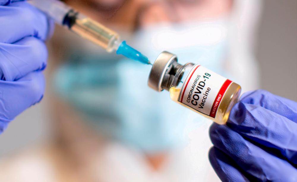 FILE PHOTO: A woman holds a small bottle labelled with a Coronavirus COVID-19 Vaccine sticker and a medical syringe in this illustration taken October 30, 2020. REUTERSpix