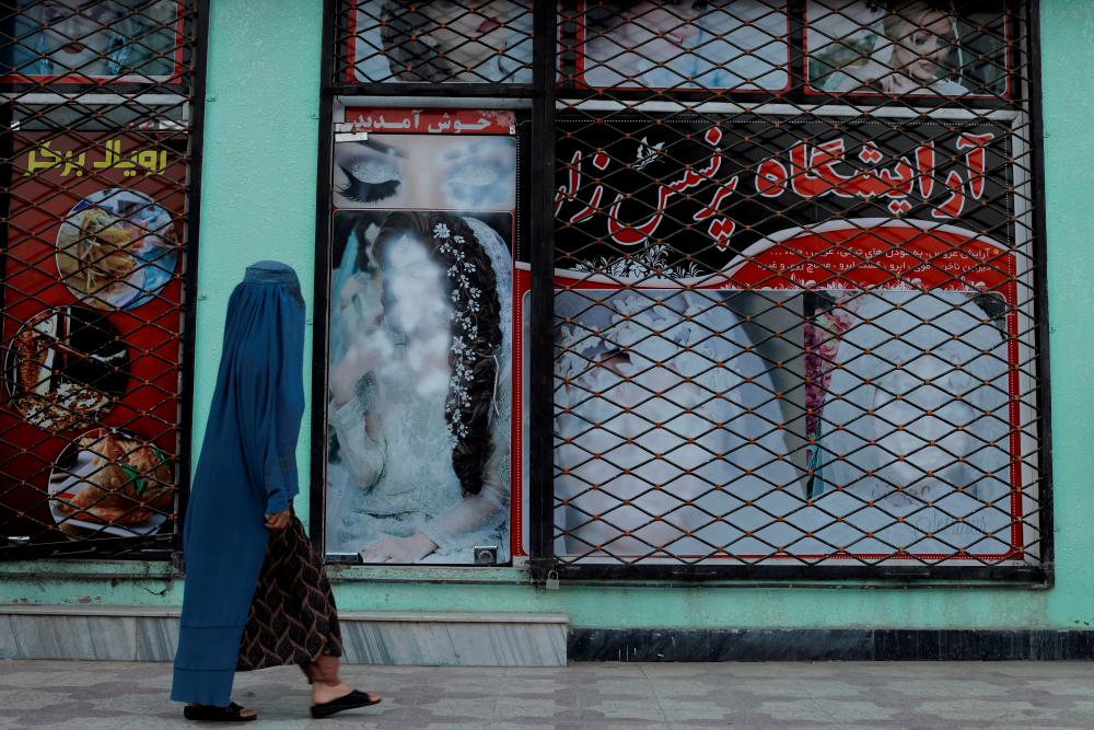 FILE PHOTO: A woman walks past a shop with defaced pictures of women in Kabul, Afghanistan October 6, 2021. REUTERS/pix