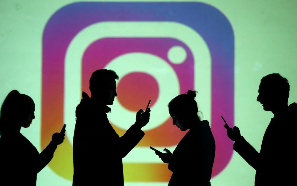Silhouettes of mobile users are seen next to a screen projection of Instagram logo in this picture illustration taken March 28, 2018. REUTERSPIX