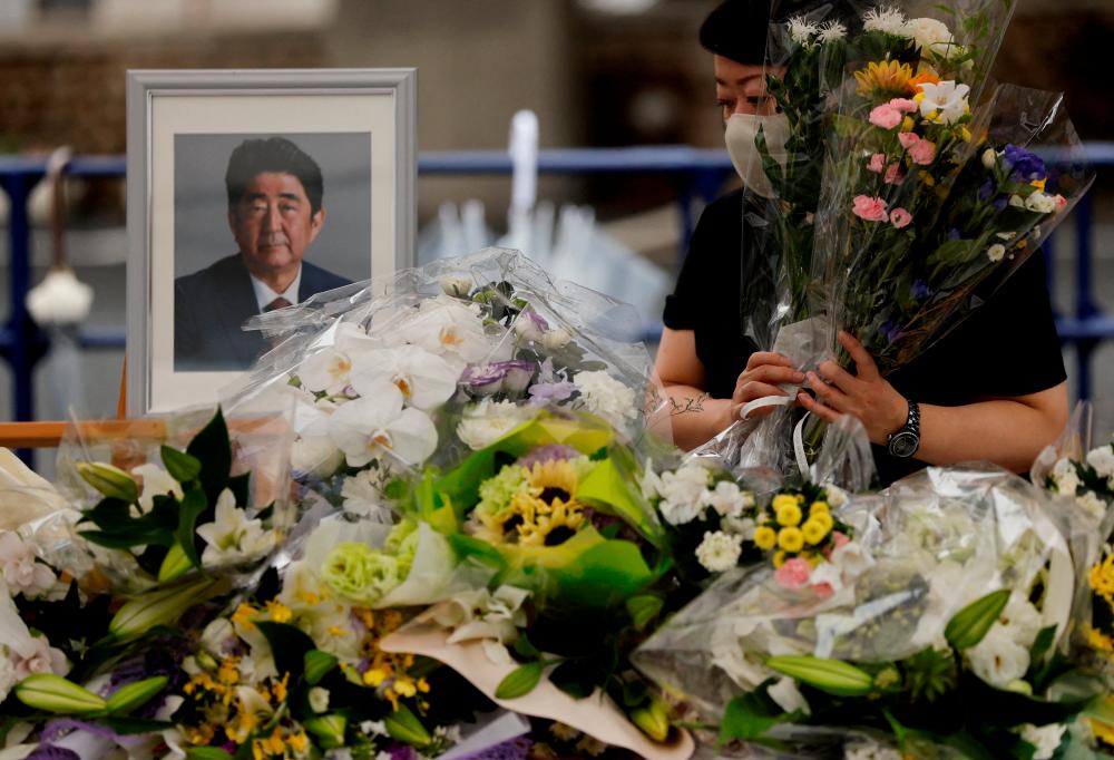 FILE PHOTO: A mourner offers flowers next to a picture of late former Japanese Prime Minister Shinzo Abe, who was shot while campaigning for a parliamentary election, on the day to mark a week after his assassination at the Liberal Democratic Party headquarters, in Tokyo, Japan July 15, 2022. REUTERSPIX