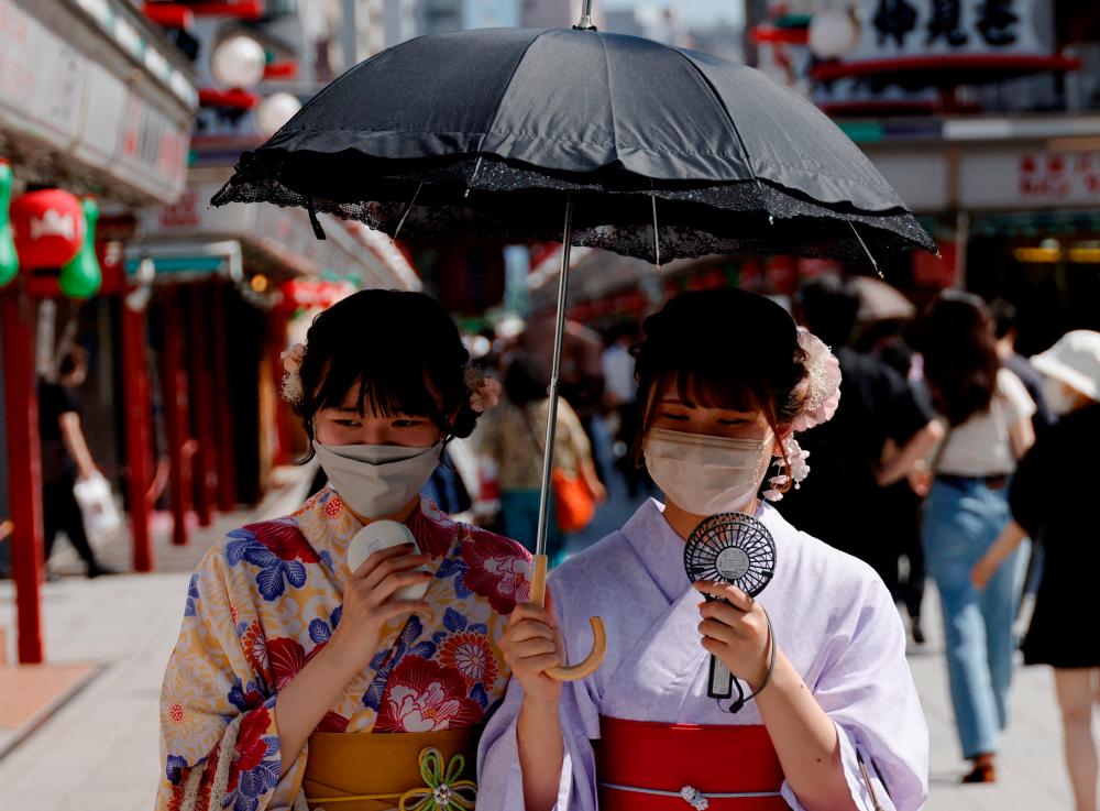 Women wearing summer kimonos use portable fans and an umbrella as they walk on the street as Japanese government issues warning over possible power crunch due to heatwave at Asakusa district in Tokyo, Japan June 29, 2022. REUTERSPIX