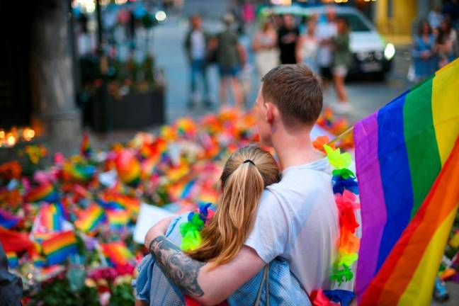 A couple stands in front of flowers and rainbow flags as people pay tribute to the victims of a shooting at the London Pub, a popular gay bar and nightclub, in Oslo/REUTERSPix