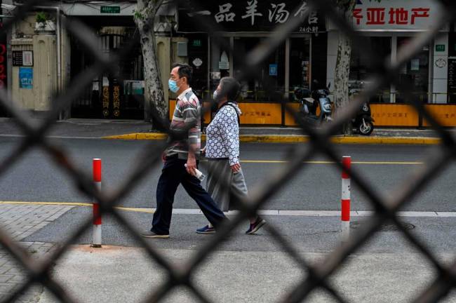 People walks on a street seen through the fence of a compound in lockdown during a Covid-19 coronavirus lockdown in the Jing'an district, in Shanghai/AFPPix