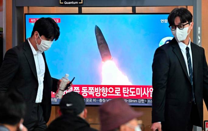 People walk past a television screen showing a news broadcast with file footage of a North Korean missile test, at a railway station in Seoul on October 4, 2022. - AFPPIX
