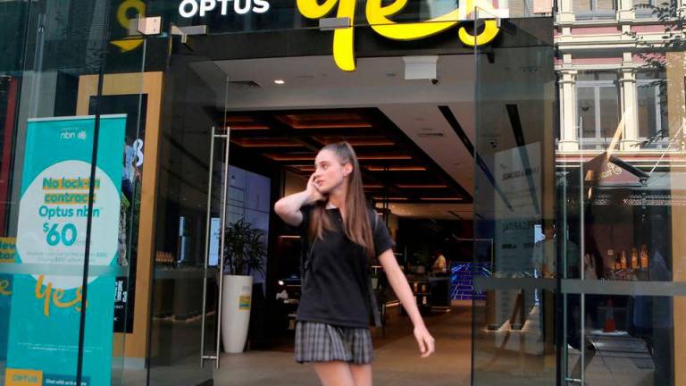 A woman uses her mobile phone as she walks past in front of an Optus shop in Sydney, Australia, February 8, 2018. REUTERSPIX
