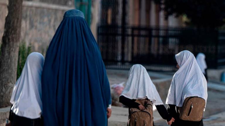 In this picture taken on August 9, 2022, an Afghan woman walks with schoolgirls going to their primary school in Kabul. AFPPIX