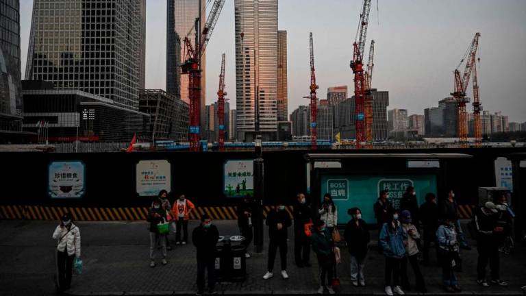 Commuters waiting at a bus stop near a construction site at central business district in Beijing. China has lent hundreds of billions of dollars to build infrastructure in developing countries. – AFPpic