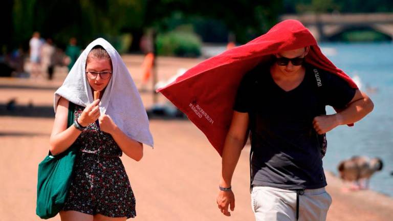 People cover their heads to shelter from the sun as they walk past the Serpentine lake in Hyde Park, west London, on July 19, 2022 as the country experiences an extreme heat wave. AFPPIX