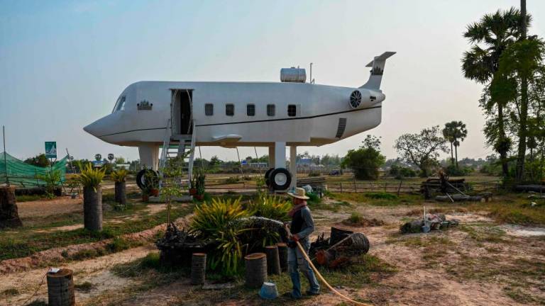 This photo taken on March 12, 2023 shows Chrach Peou spraying water in a garden in front of his house that is shaped like an airplane in Siem Reap province/AFPPix