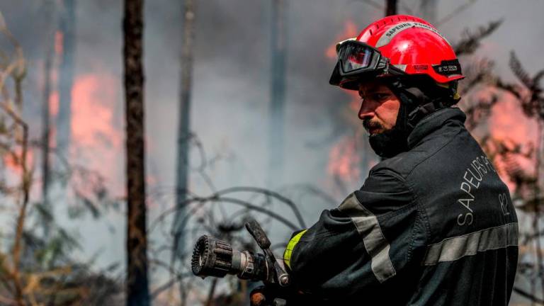 A French firefighter holds a nozzle during a wildfire near Belin-Beliet, southwestern France, on August 13, 2022. AFPPIX