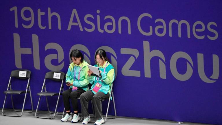 Volunteers sit in front of a sign of the Hangzhou Asian Games in the women's team preliminary round of table tennis during the 2022 Asian Games in Hangzhou//AFPix