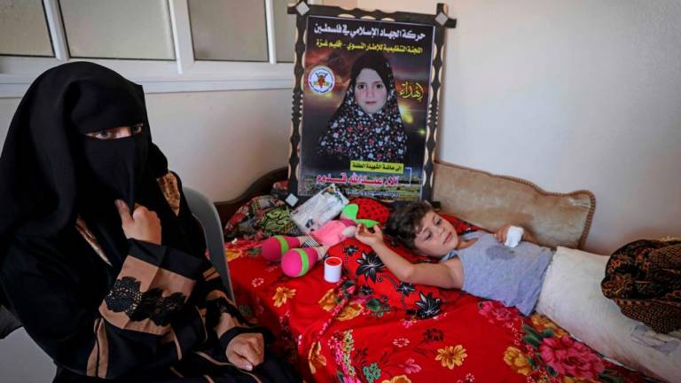 Palestinian mother Rasha Qadoom sits by her wounded child Rayed near a poster depicting her five-year-old daughter Alaa killed during the latest conflict between Israel and Palestinian militants, in Gaza on August 9, 2022. AFPPIX