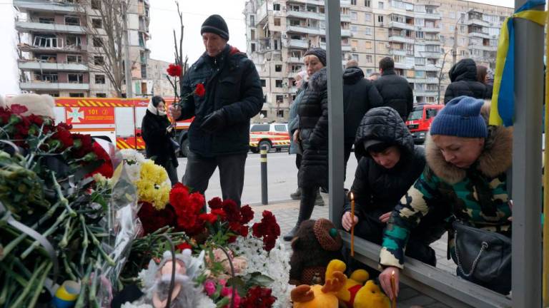 Local residents lay flowers at a bus stop in front of the residential building in the Ukrainian city of Dnipro on January 22, 2023, destroyed as a result of a missile strike on January 14. AFPPIX