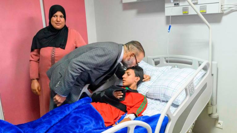 This handout picture taken and released on September 12, 2023 shows Moroccan King Mohammed VI kissing the head of an injured victim at “Mohammed VI” University Hospital center in Marrakech as he pays a hospital visit to victims of the earthquake that rocked the North African country last week, killing at least 2,900 people, state media reported/AFPPix