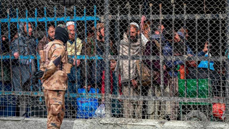 In this picture taken on February 2, 2023, A Taliban security personnel talks with Afghan people waiting behind a fenced corridor before they cross into Pakistan at the zero point Torkham border crossing between Afghanistan and Pakistan, in Nangarhar province. AFPPIX