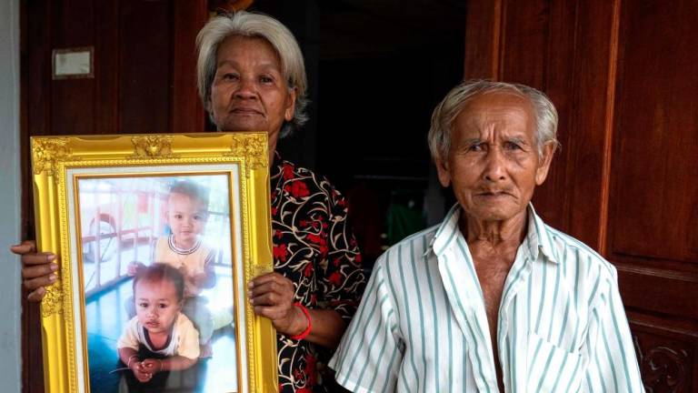 This photo taken on August 31, 2023 shows Pranee Tunawa standing beside his wife Thongsa Tunawa (L) holding a photo of their three-year-old grandsons Aphiwut “Titan” Manochart and Chaiyanon “Asean” Thongpuban, who were killed in a nursery mass shooting on October 6, 2022. AFPPIX