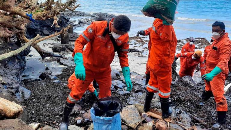 This handout photo taken on March 8, 2023 and released by the Philippine Coast Guard (PCG) shows coast guard personnel and volunteers collecting debris covered with oil during a clean-up along the coast in Pola, Oriental Mindoro Province, days after an oil spill from a sunken tanker. AFPPIX