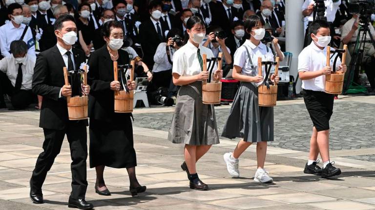 A-bomb survivors and representatives of bereaved families carry offerings of water during a memorial ceremony at the Peace Park in Nagasaki on August 9, 2022, on the 77th anniversary of the atomic bombing during WWII. - AFPPIX