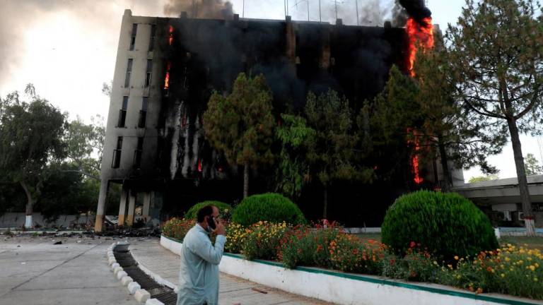 FILE PHOTO: A man speaks on his mobile as fire and smoke billow from a Radio Pakistan building after it was set afire by the supporters of Pakistan's former Prime Minister Imran Khan during a protest against his arrest, in Peshawar, Pakistan, May 10, 2023. REUTERSPIX
