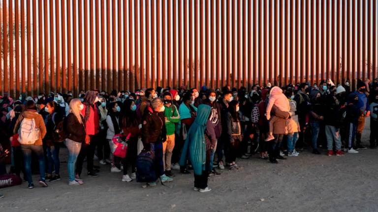 Migrants seeking asylum in the US, mostly from Venezuela, stand near the border fence while waiting to be processed by the US border patrol after crossing the border from Mexico at Yuma, Arizona, US, January 23, 2022. REUTERSPIX