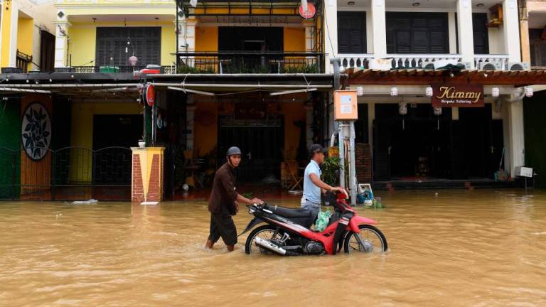 People push a motorbike in a flooded street following the passage of typhoon Noru in Hoi An city, Quang Nam province on September 28, 2022. AFPPIX