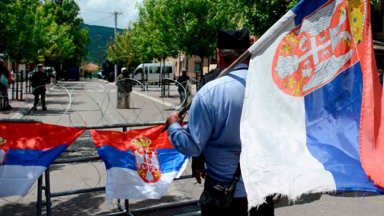 A man holding a Serbian flag looks on as he stands in front of NATO-led Kosovo Force (KFOR) soldiers in full riot gear standing behind a barbed wire perimeter around the municipal building in Zvecan. AFPPIX