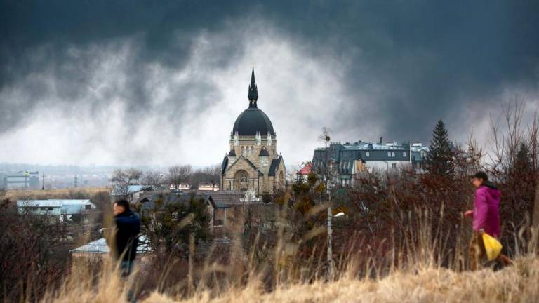 FILE PHOTO: People walk in front of a church as smoke rises after an air strike in the western Ukrainian city of Lviv, on March 26, 2022. AFPPIX