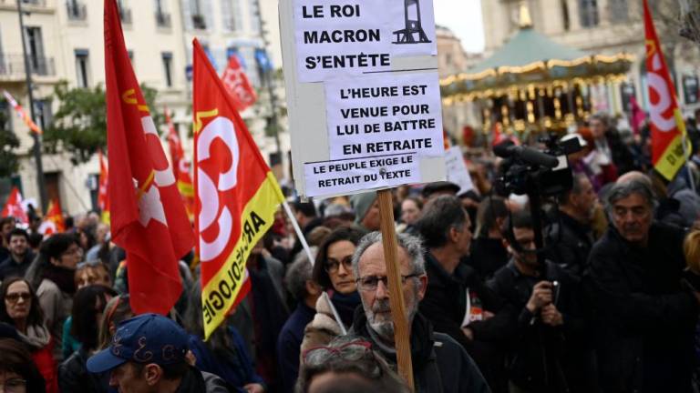 Protesters march holding a placard which reads as “Pensions. Macron the King is stubborn. Time for him to retreat from the scene. AFPPIX