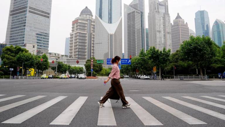 File photo: A pedestrian wearing a face mask crosses a road in front of office towers in Lujiazui financial district, after the lockdown placed to curb the coronavirus disease (Covid-19) outbreak was lifted in Shanghai, China June 1, 2022. REUTERSpix