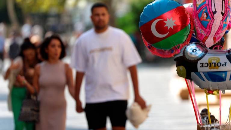 A couple walk past a balloon vendor displaying an Azerbaijani flag balloon in Baku//AFPix