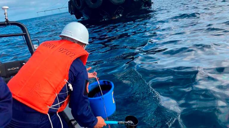In this handout photo received from the Philippine Coast Guard and taken on March 2, 2023, a coast guard personnel collects water sample from of an oil spill in the waters off Naujan, Oriental Mindoro. AFPPIX