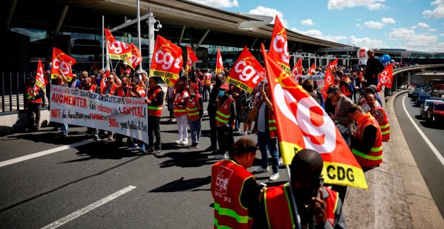 FILE PHOTO: Paris-Charles de Gaulle airport employees on strike hold French CGT labour union flags as they walk outside the Terminal 2F during a protest against low wages as inflation hits France, at the Paris-Charles de Gaulle airport in Roissy, near Paris, France, July 1, 2022. REUTERSpix