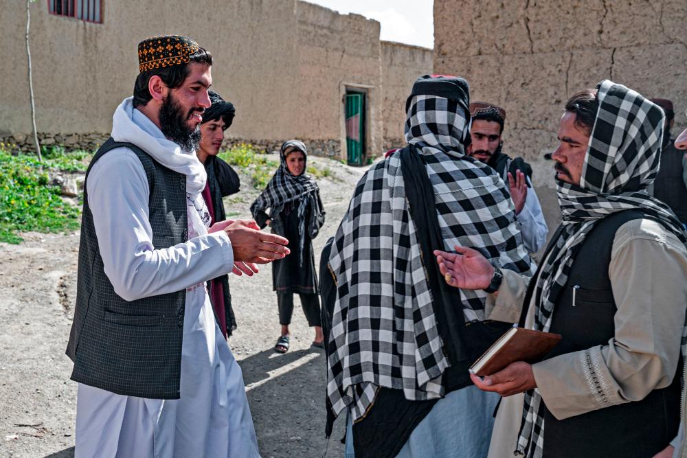 In this photo taken on May 25, 2023, Taliban-trained suicide bomber Ismail Ashuqullah (L) speaks with Taliban's General Directorate of Intelligence (GDI) after an interview with AFP in Otarhi village in Tangi valley of Saydabad district - AFPPIX