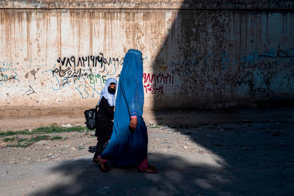 In this picture taken on August 9, 2022, an Afghan woman and a girl walk to a primary school in Kabul. - AFPPIX