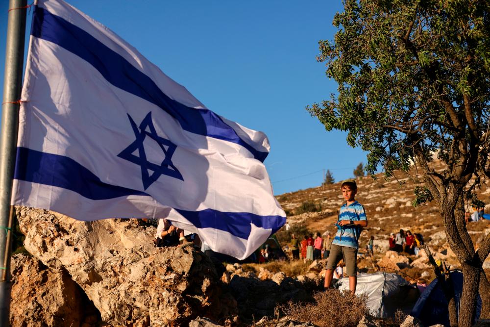 An Israeli boy stands near an Israeli flag during a gathering of the Israeli settlement movement making a bid to set a new settlement close to Kiryat Arba, a Jewish settlement in Hebron in the Israeli-occupied West Bank July 20, 2022. REUTERSPIX