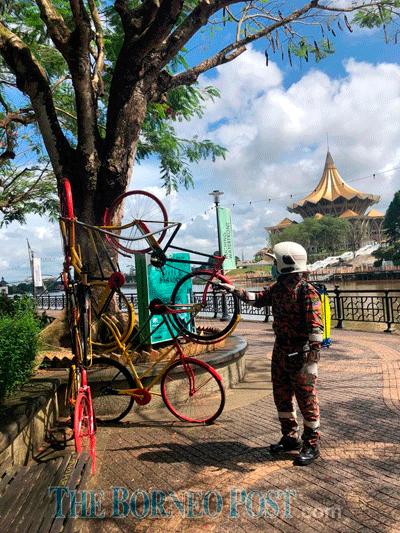 $!A fire personnel sprays an art piece at Kuching Waterfront when carrying out sanitisation works in this file photo. — The Borneo Post