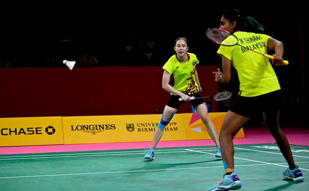 Muralitharan Thinaah plays a shot behind her back with Koon Le Pearly Tan as they play against England's Chloe Birch and Lauren Smith in their women's doubles gold medal badminton match on day eleven of the Commonwealth Games at the NEC arena in Birmingham, central England, on August 8, 2022. AFPPIX