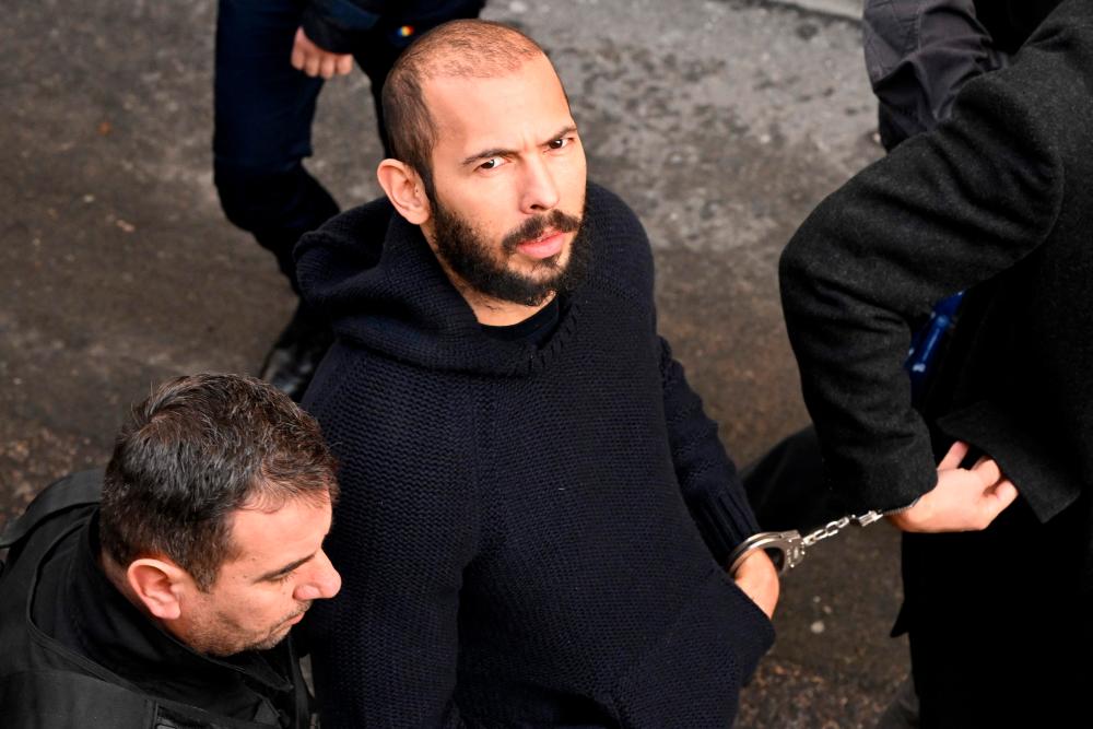 (FILES) In this file photo taken on February 01, 2023 British-US influencer Andrew Tate arrives handcuffed and escorted by police at a courthouse in Bucharest on February 1, 2023 to hear the court decision on his appeal against pre-trial detention for alleged human trafficking, rape and forming a criminal group. AFPPIX