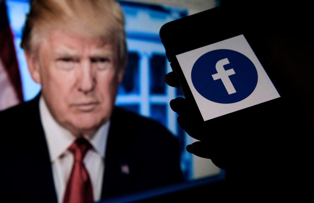 (FILES) In this file illustration photo taken on May 4, 2021, a phone screen displays a Facebook logo with the official portrait of former US President Donald Trump on the background in Arlington, Virginia. AFPPIX