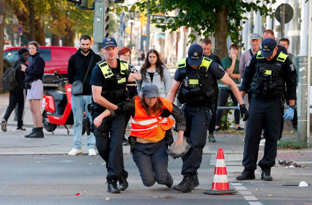 Policemen carry away a climate activist who has a piece of road surface on her hand as she glued herself to the street in order to draw attention to the climate emergency as police dissolves a blockade of the Letzte Generation (Last Generation) movement, on September 18, 2023 in Berlin. - AFPPIX