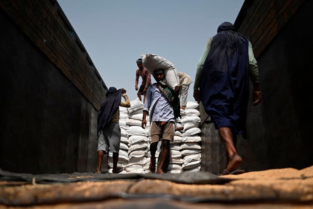 Workers carry sacks of wheat to load on a freight train at Chawa Pail railway station in Khanna, Punjab state, on May 19, 2022. AFPPIX