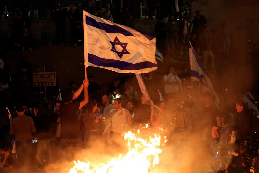 Protesters block a road and hold national flags as they gather around a bonfire during a rally against the Israeli government's judicial reform in Tel Aviv, Israel on March 27, 2023. AFPPIX