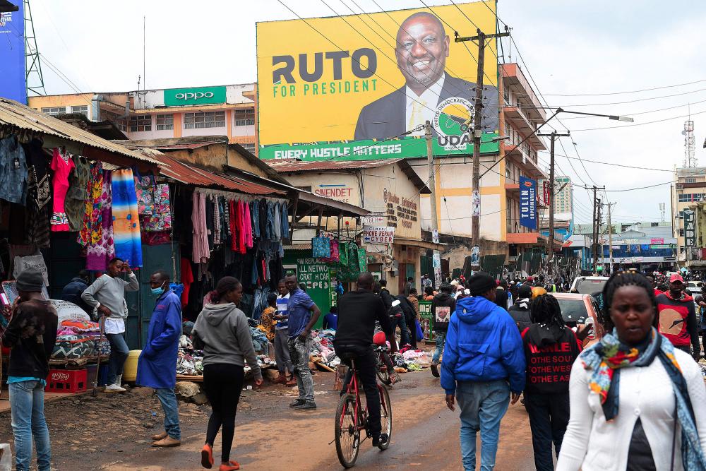 Pedestrians walk in a street next to a billboard of Kenya's Deputy President William Ruto and presidential candidate for the United Democratic Alliance (UDA) and Kenya Kwanza political coalition, in Eldoret, on August 13, 2022. - AFPPIX