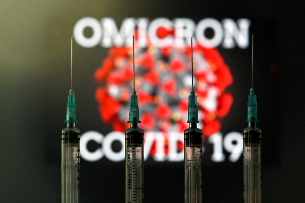 An illustration picture taken in London on December 2, 2021 shows four syringes and a screen displaying the word 'Omicron', the name of the new covid 19 variant, and an illustration of the virus. AFPpix