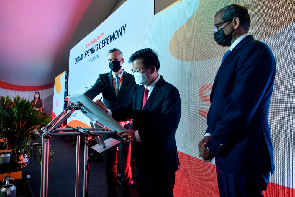 Chow signing a plaque to mark the opening of Smith &amp; Nephew Penang’s manufacturing facility in Batu Kawan today. Also present are Smith &amp; Nephew CEO Deepak Nath (right) and Smith &amp; Nephew Operations Malaysia Sdn Bhd managing director and site leader Mark Arthun. BERNAMApix