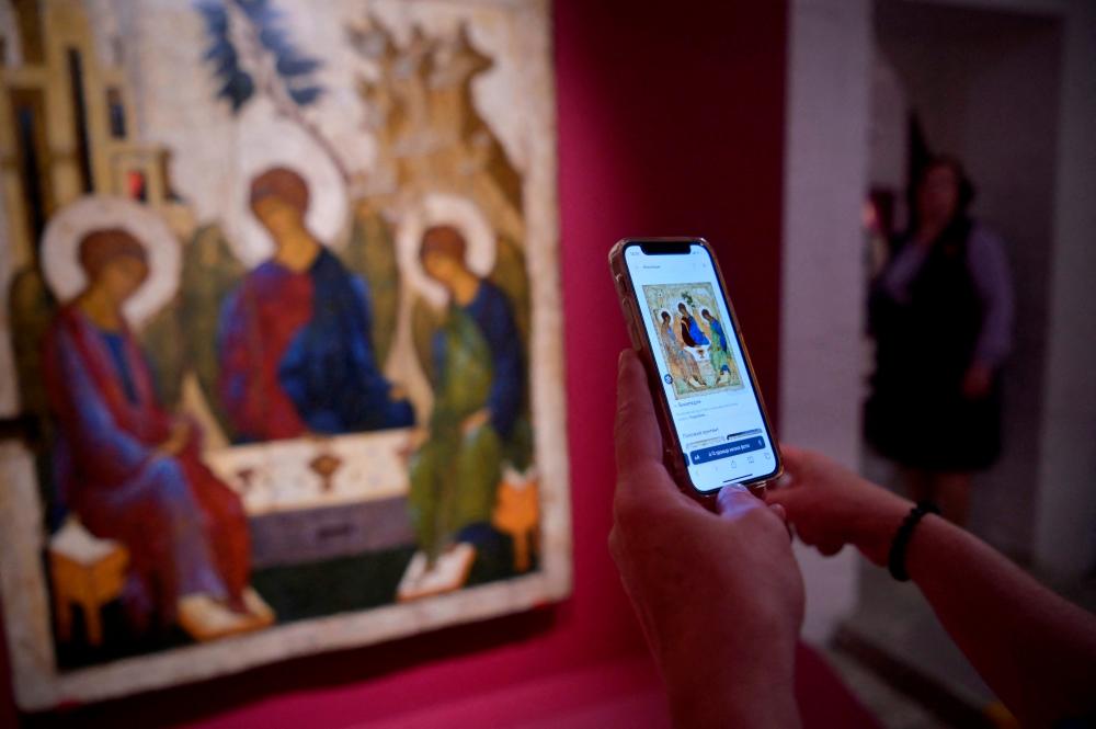 A visitor compares the Andrei Rublev’s “Trinity” icon displayed on a smartphone screen with the late 15th century icon “Holy Trinity” displayed at the Central Andrey Rublev Museum of Ancient Russian Culture and Art in Moscow on May 22, 2023. AFPPIX