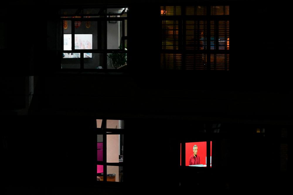 A television screen (bottom R) seen through the window of a residential apartment shows a live broadcast of Singapore's Prime Minister Lee Hsien Loong delivering his National Day Rally speech in Singapore on August 21, 2022. AFPPIX