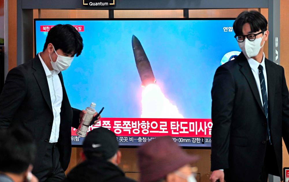 People walk past a television screen showing a news broadcast with file footage of a North Korean missile test, at a railway station in Seoul on October 4, 2022. - AFPPIX