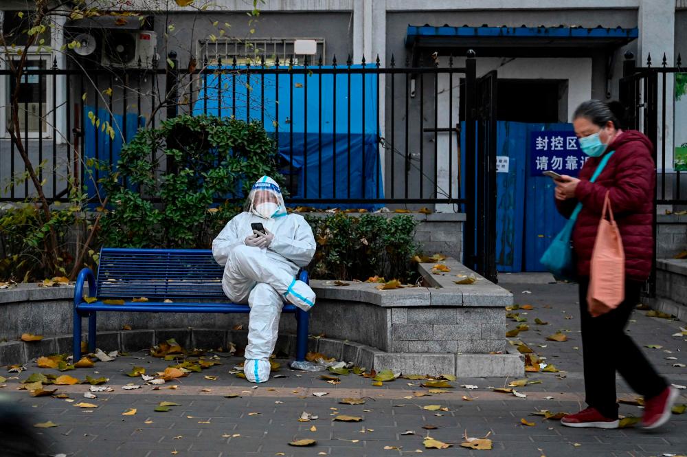 A man clad in personal protective equipment sits outside a residential building under lockdown due to Covid-19 restrictions in Beijing on Tuesday, Nov 22. Analysts now are cutting forecasts for China’s year-end oil demand. – AFPpic