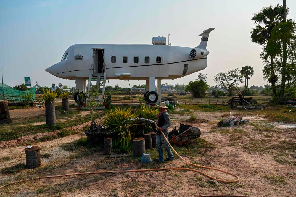 This photo taken on March 12, 2023 shows Chrach Peou spraying water in a garden in front of his house that is shaped like an airplane in Siem Reap province/AFPPix